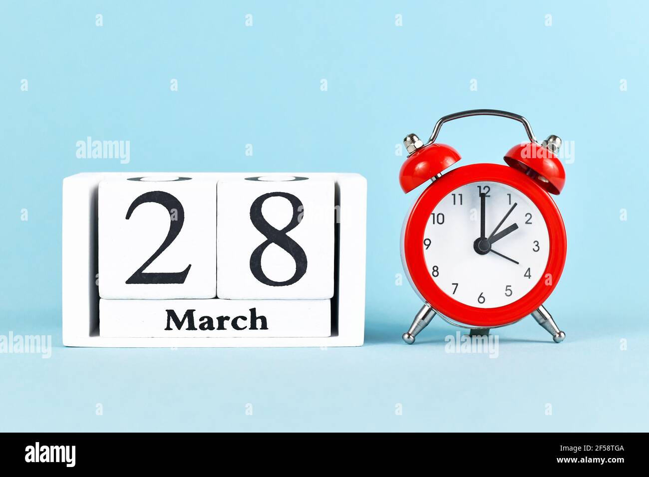 Concept for time change for daylight saving summer time in Europe on March 28th with red alarm clock and calendar on blue Stock Photo