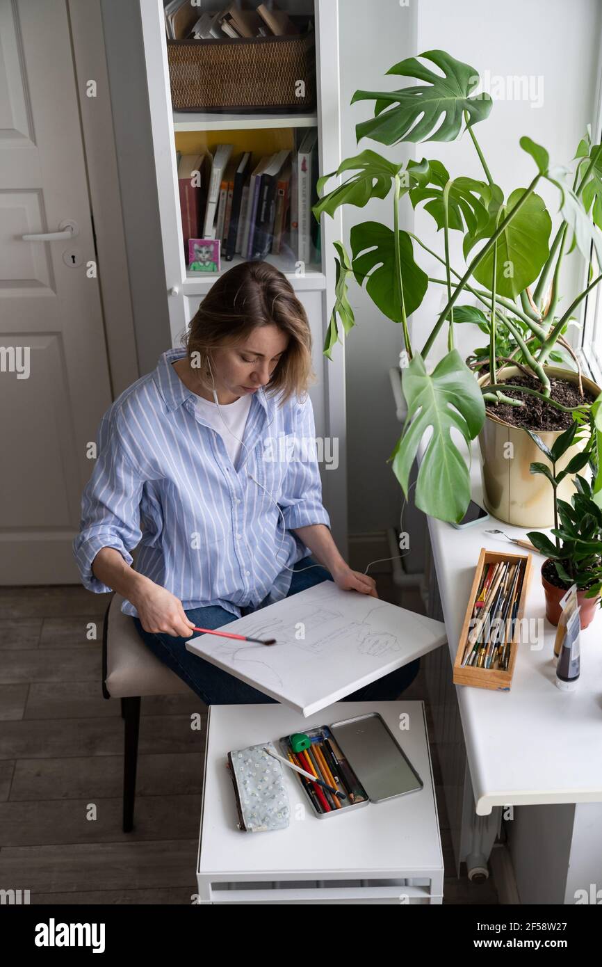 Woman artist paints a picture on canvas, makes pencil sketches, erases