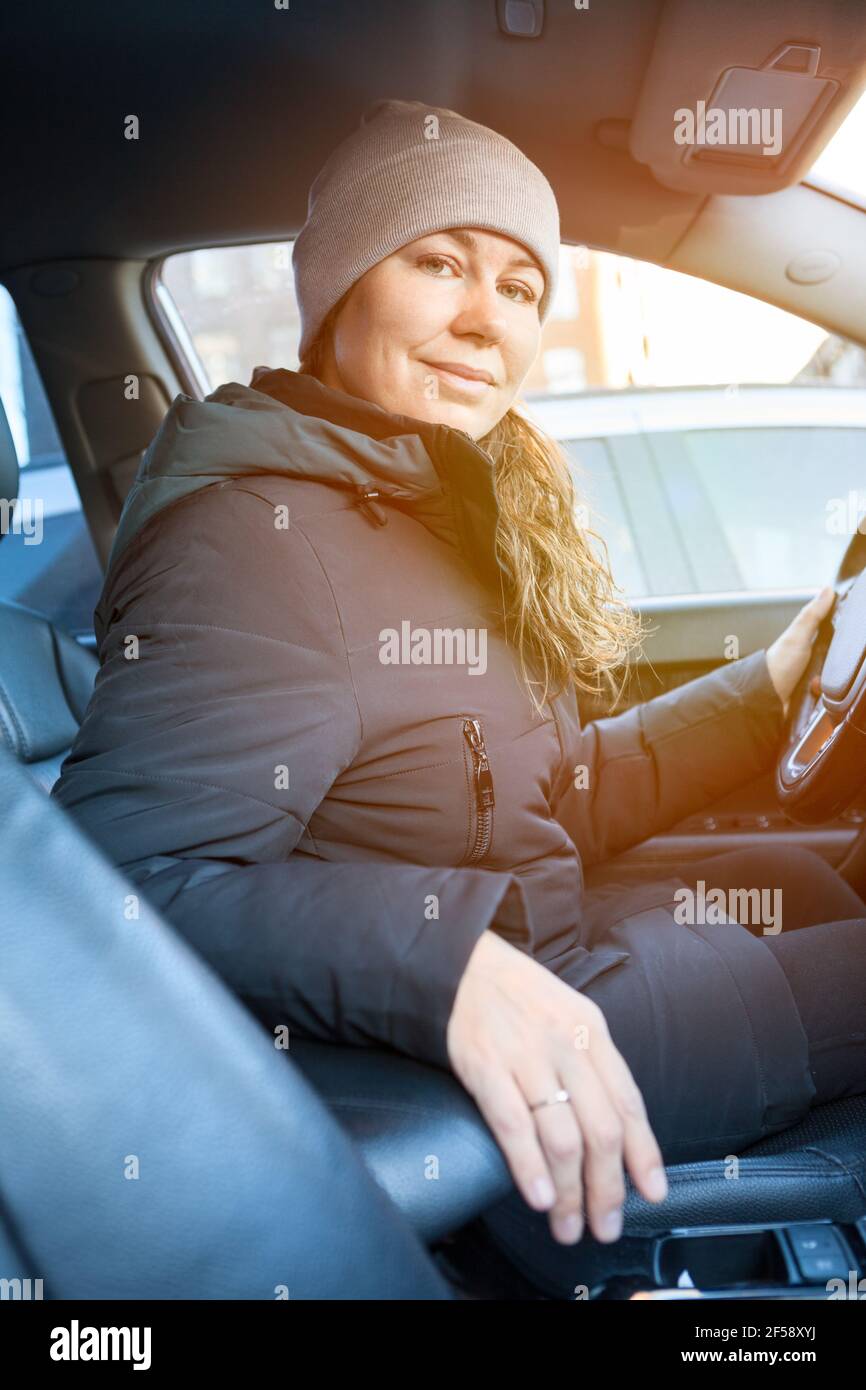 Young Caucasian woman starts driving a car in winter evening, looking at camera Stock Photo