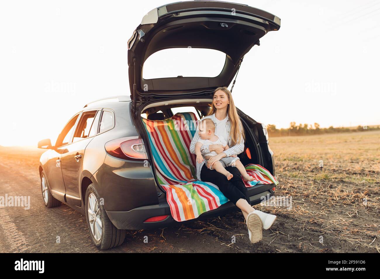 Happy family, a young mother with a child sitting in the trunk of a car ...