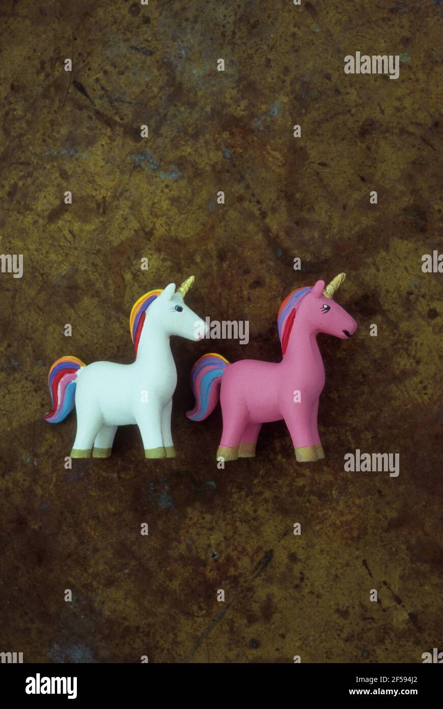 Models of one white and one pink unicorns with rainbow tails and manes and gold horns standing head to tail Stock Photo