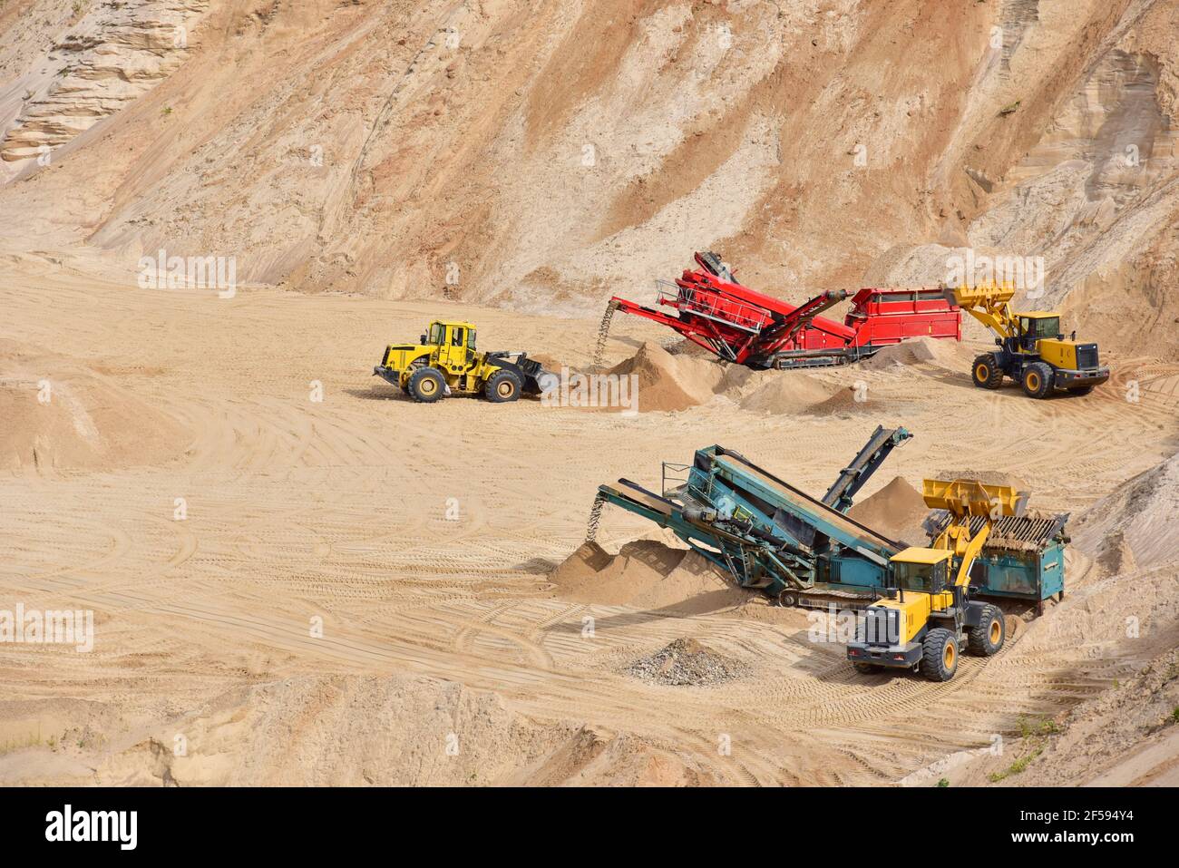Wheel front-end loader loads sand into a dump truck. Heavy machinery in the mining quarry, excavators and trucks. Mobile jaw crusher plant with belt c Stock Photo