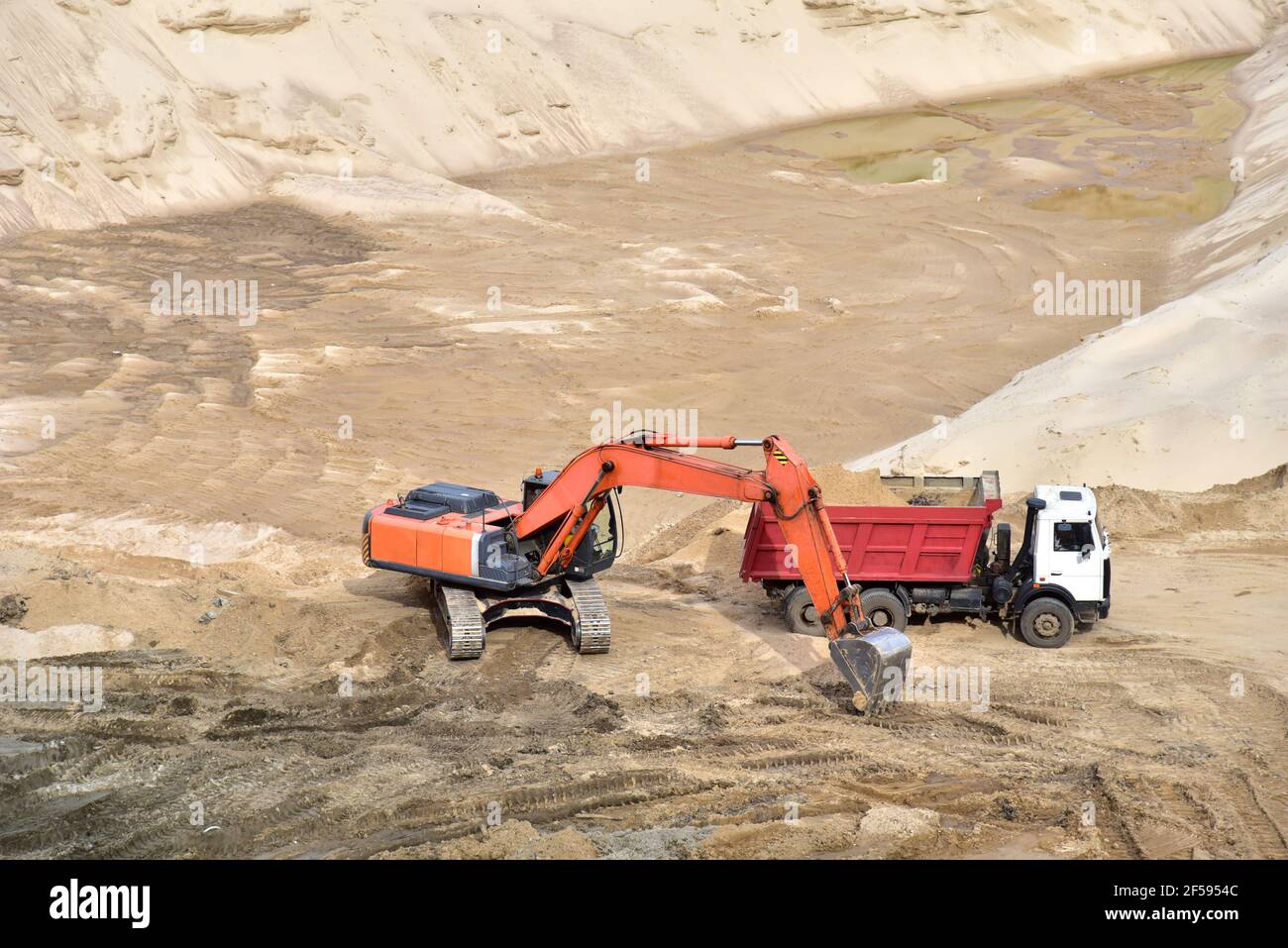 Excavator loading sand into heavy dump truck at mining quarry site