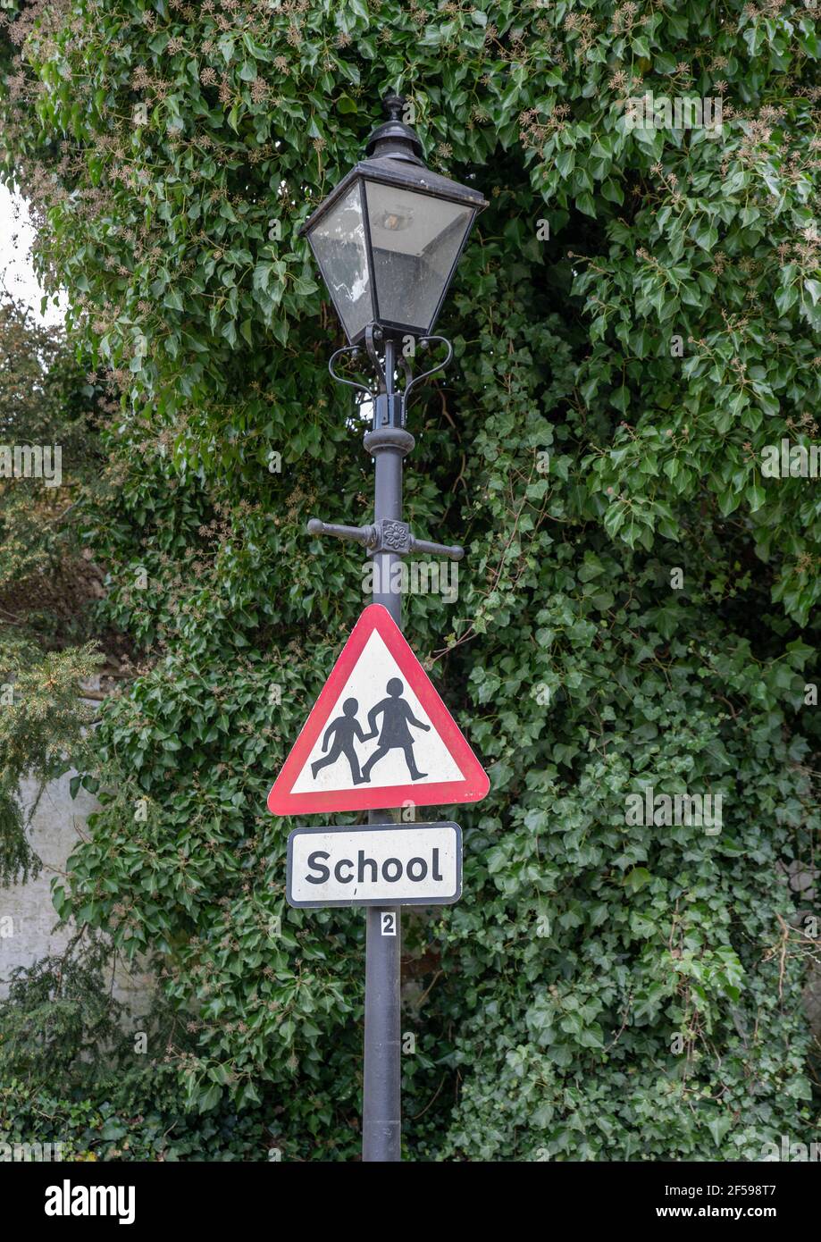 Red and white triangle school sign with children holding hands on an ornate street light lamppost. Stock Photo