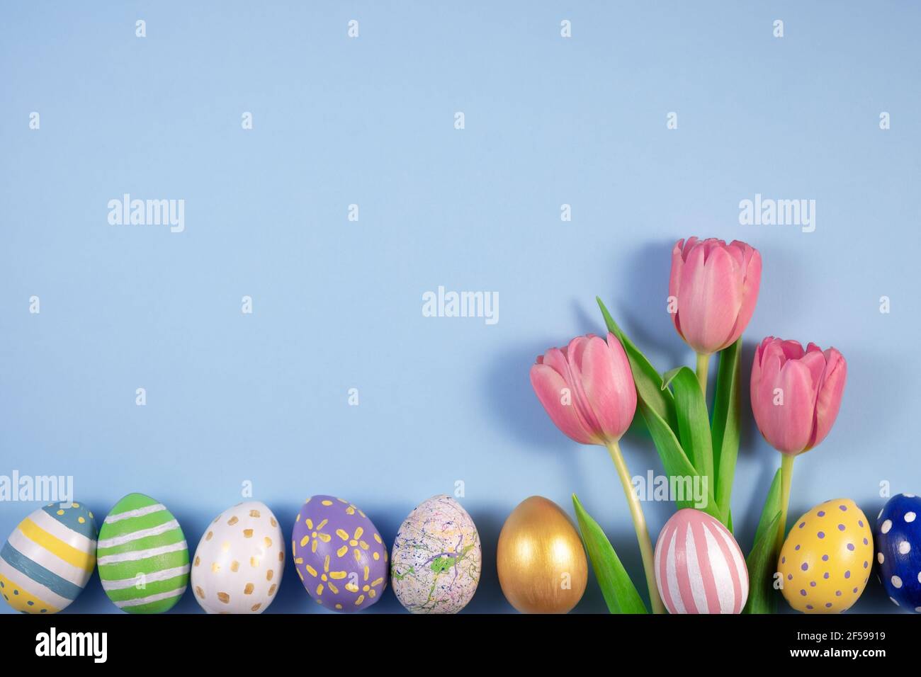 Pink tulips flowers and colourful eggs on blue background. Card for Happy Easter. Waiting for spring. Greeting card. Hello spring and easter concept. Stock Photo
