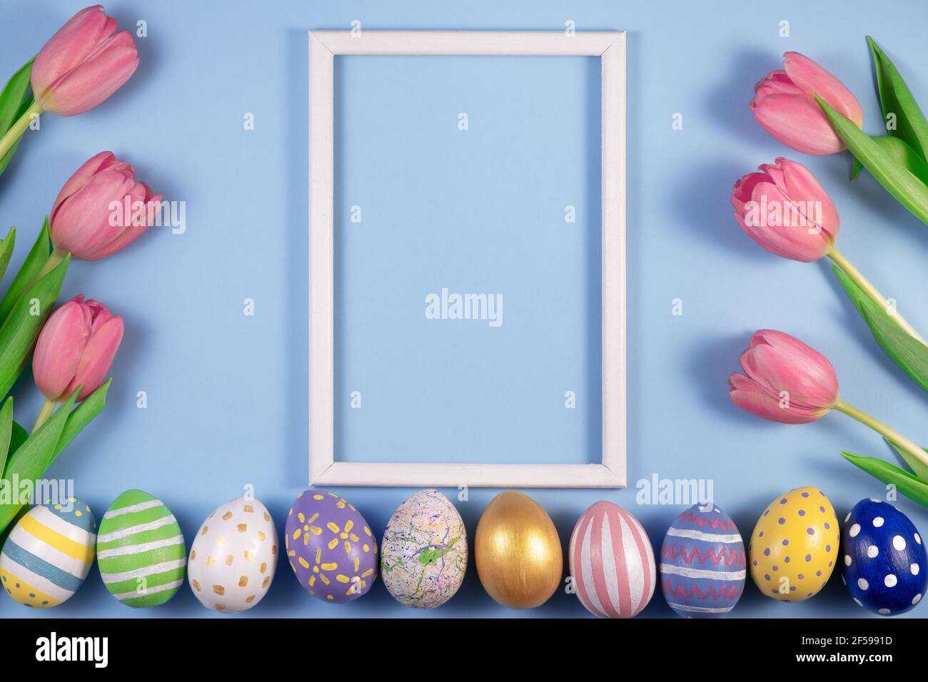 Tulips flowers and Easter eggs with wooden frame on blue background. Card for Happy Easter. Waiting for spring. Greeting card. Hello spring and easter Stock Photo