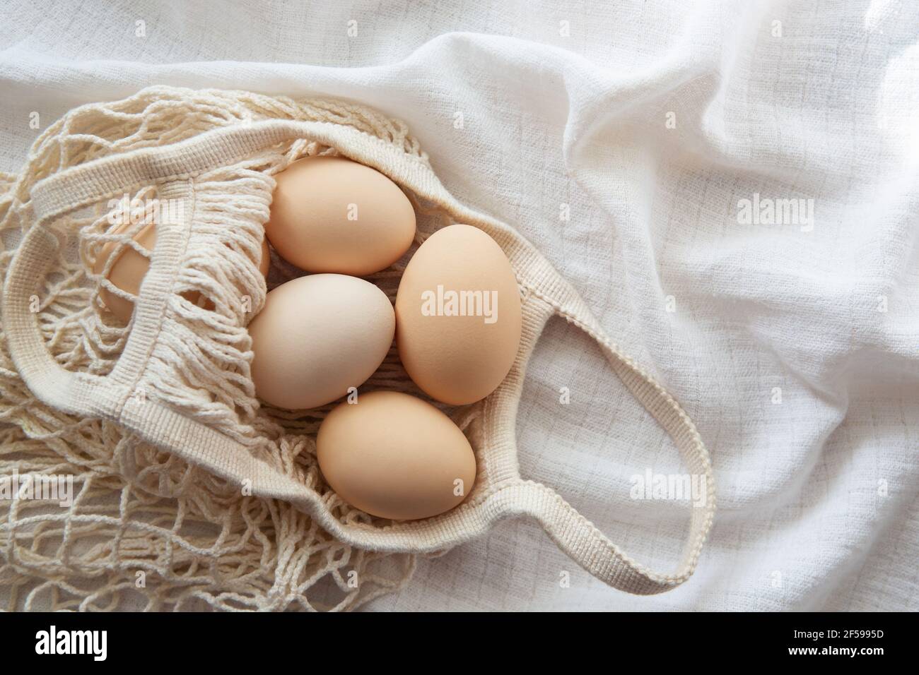 Chicken eggs in a string bag on white background, selective focus. Happy easter background. Stock Photo