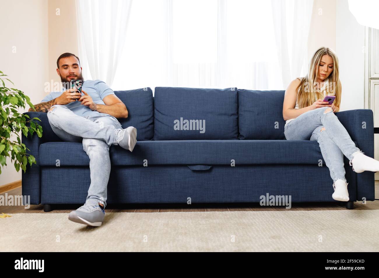 Scolded couple sitting on opposite sides of the couch using their
