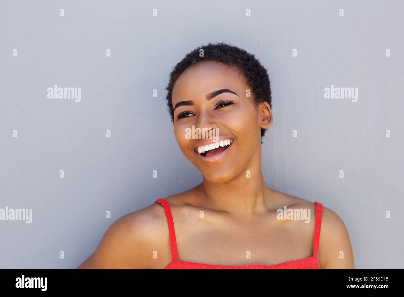 Close up portrait of attractive young black woman laughing against gray ...