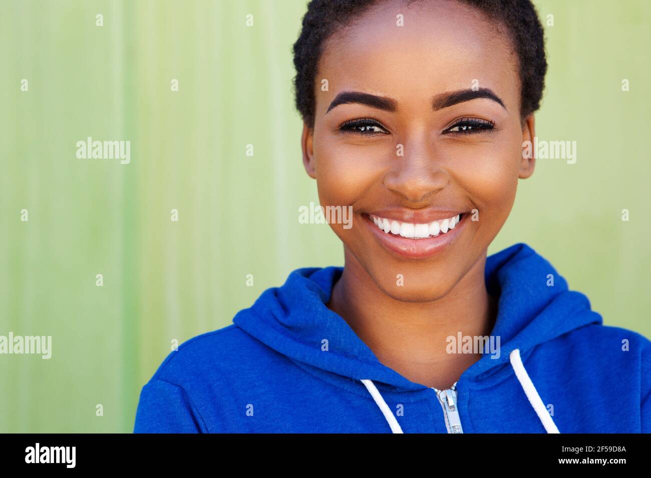 Close up portrait of smiling young black woman against green background ...