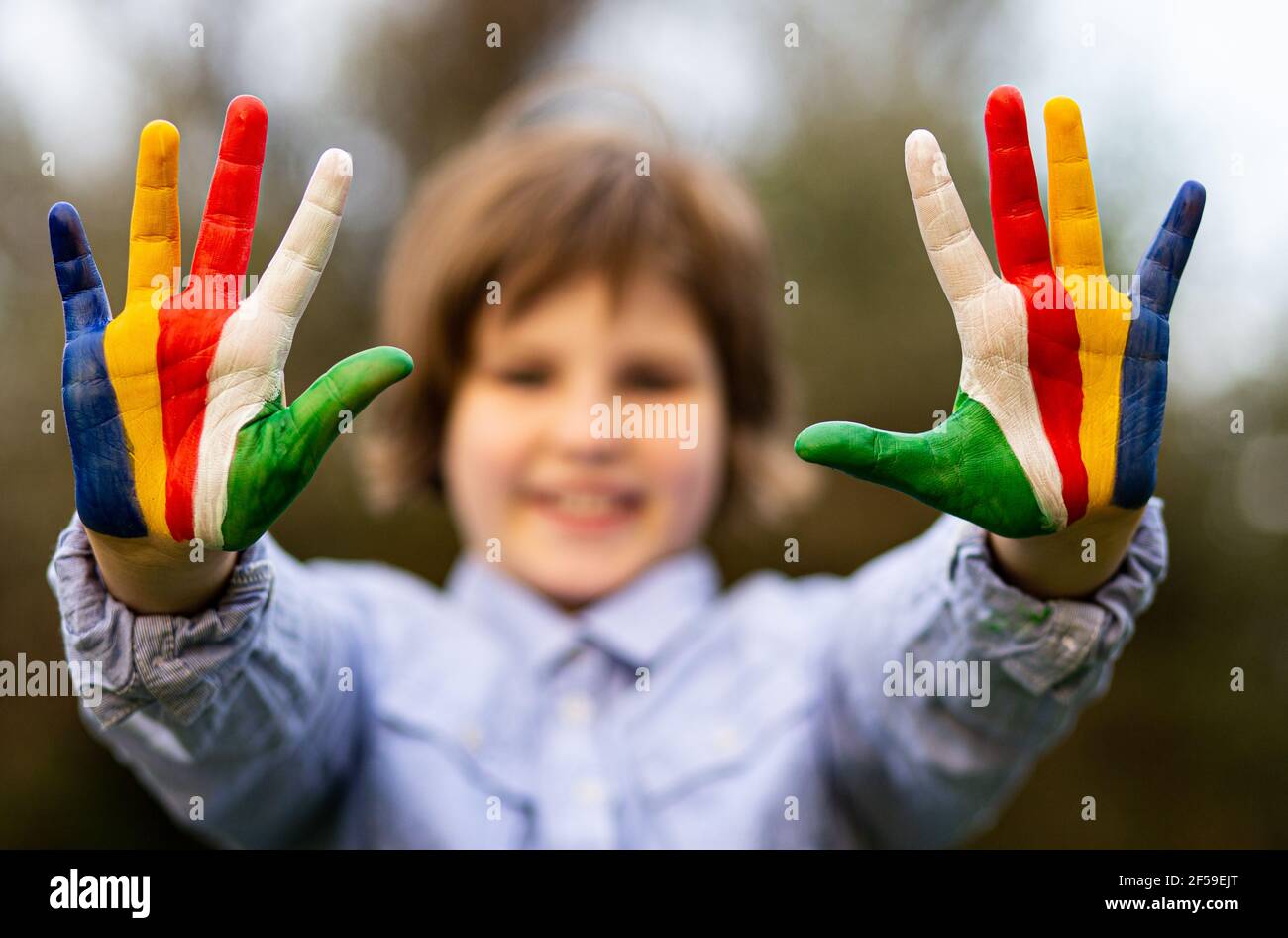Outdoor portrait of cheerful kid girl show hello gesture with hands painted in rainbow colors. Focus on hands Stock Photo