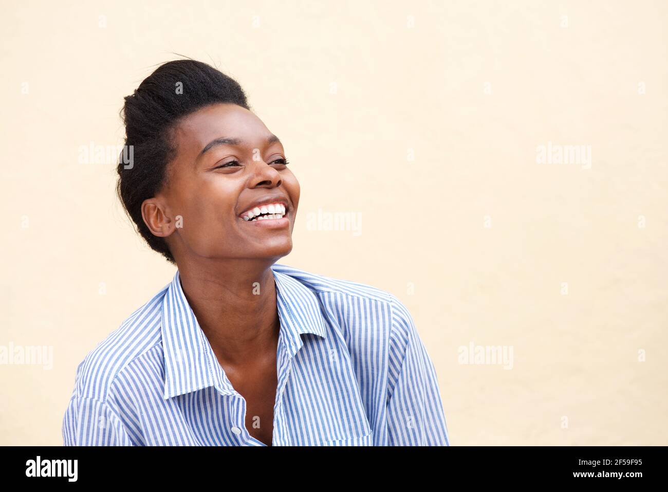 Close up portrait of beautiful young black woman laughing against wall ...