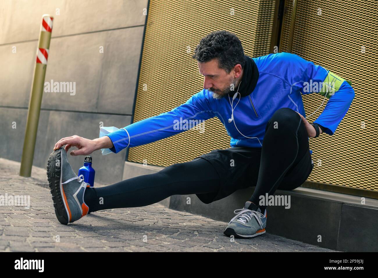 Male doing stretching and listening music after workout. Man resting during city jogging. Runner with mobile phone connected to a smart watch recordin Stock Photo