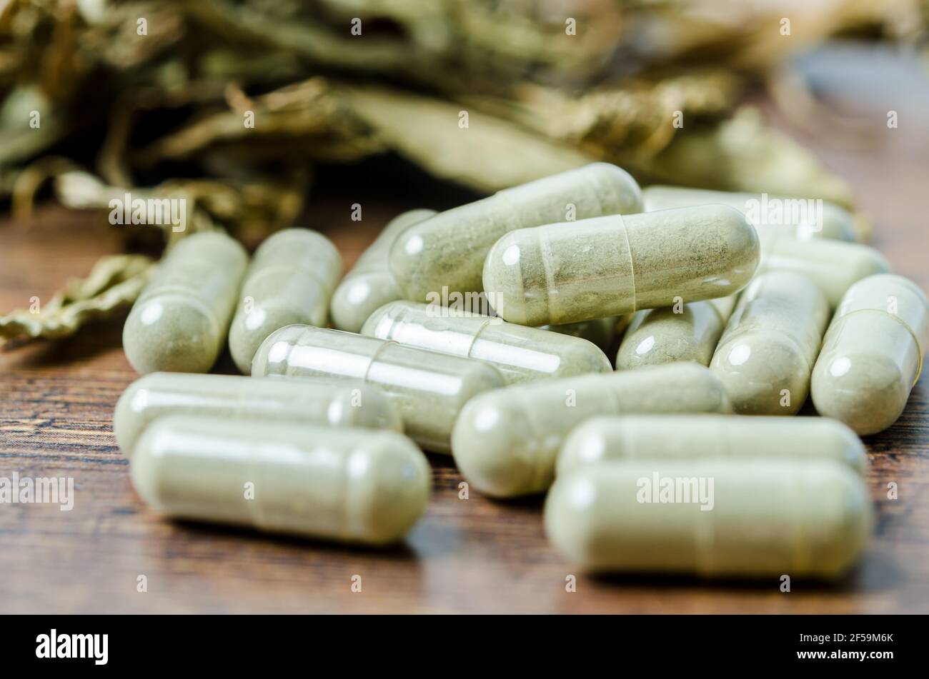 Pile of herbal medicine in capsules with herb dry leaf on wooden