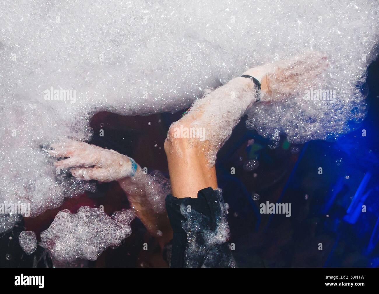 Hands of a man play with foam at a foam party in a Stock