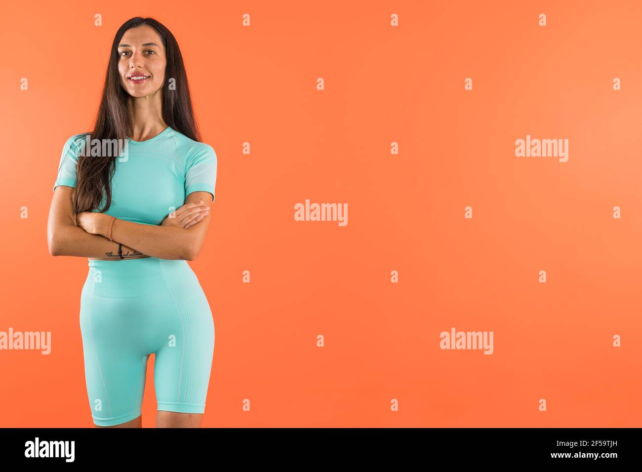 Winsome Caucasian woman with turquoise workout outfit and crossed arms posing with copy space in studio Stock Photo