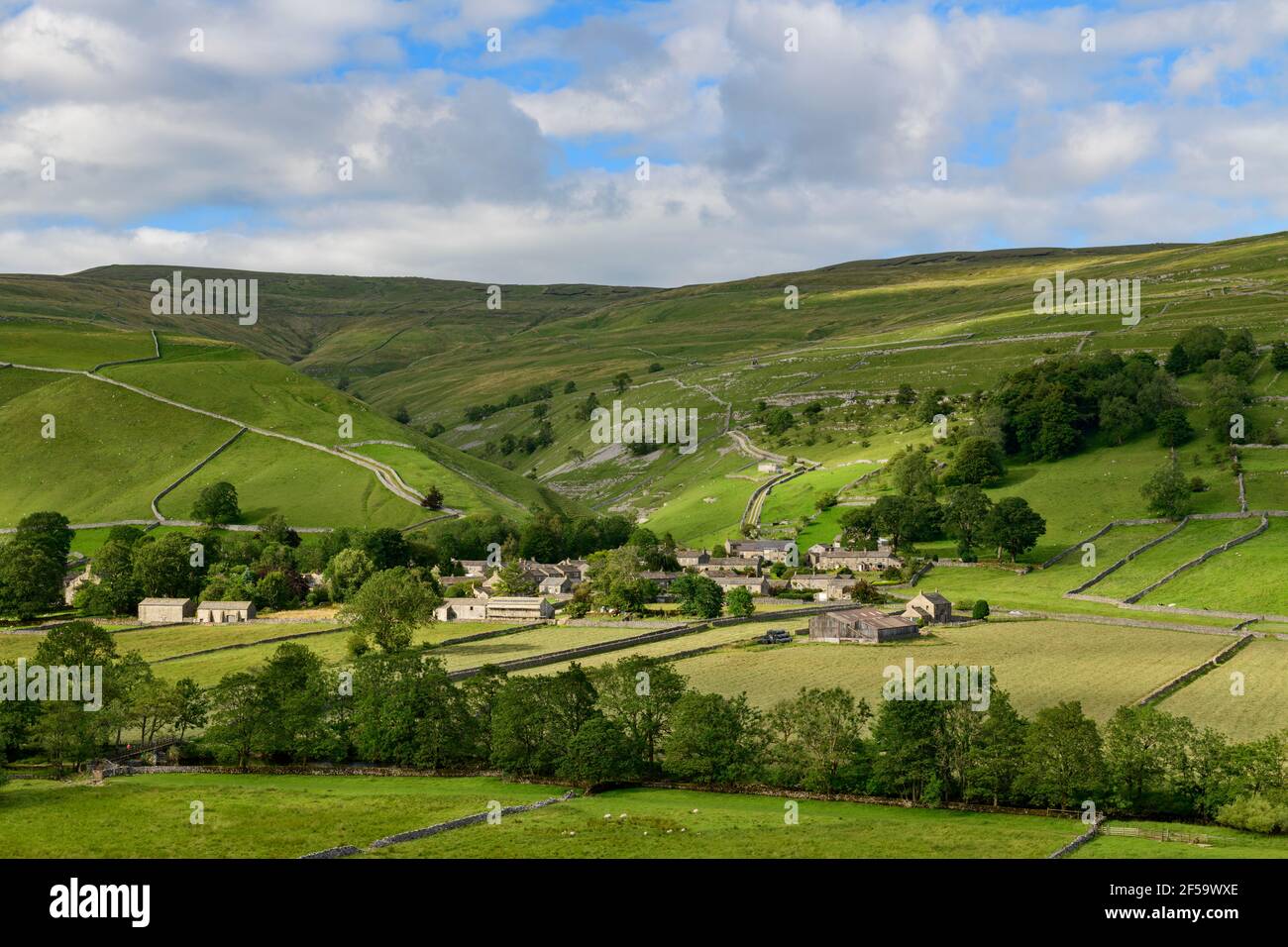 Picturesque Dales village (stone houses) nestling in sunlit valley by fields, hills, hillsides & steep-sided gorge - Starbotton, Yorkshire England UK. Stock Photo