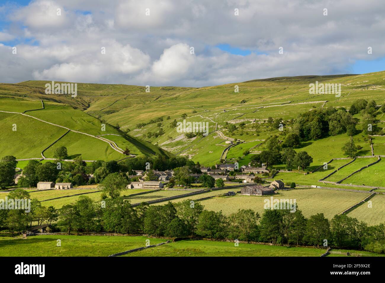 Picturesque Dales village (stone houses) nestling in sunlit valley by fields, hills, hillsides & steep-sided gorge - Starbotton, Yorkshire England UK. Stock Photo