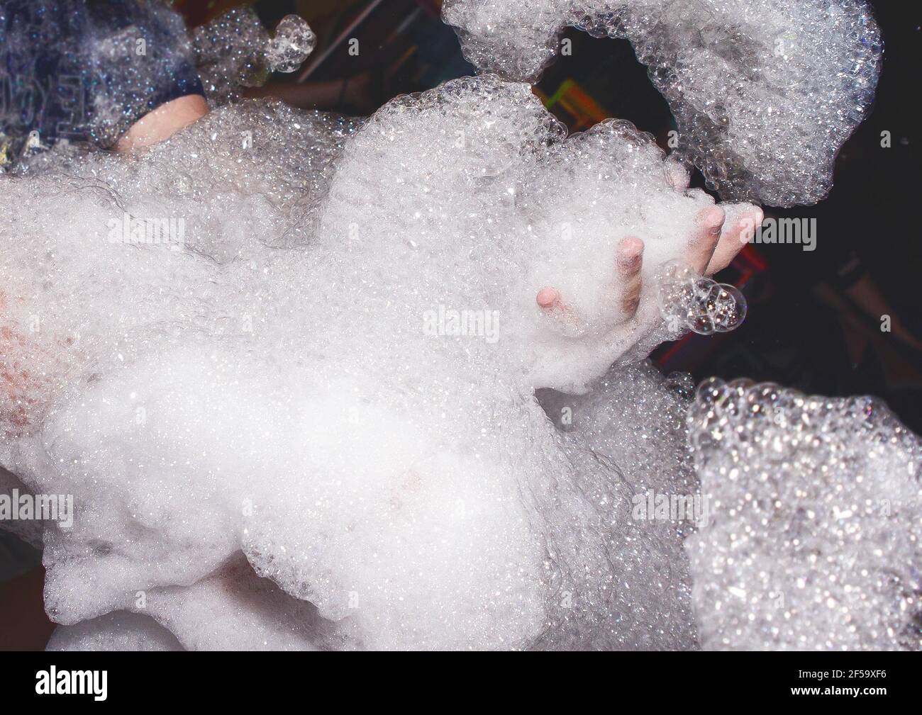 Lots of soap suds in the hands of a man at a foam party in a nightclub background. Stock Photo