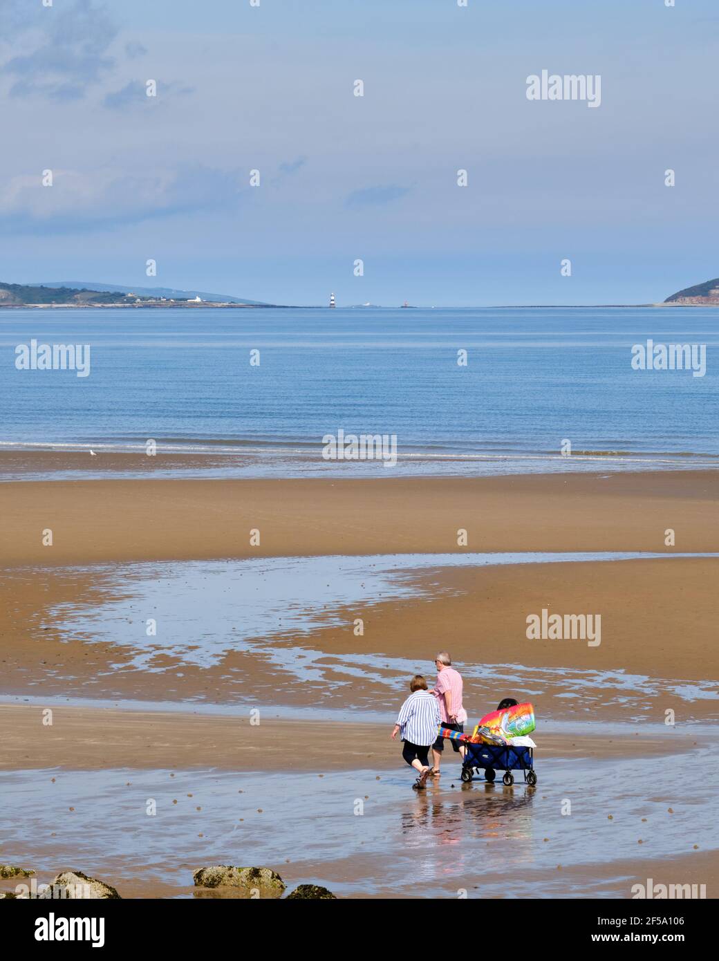 A couple head to the beach with a trolley loaded with supplies for a day at the seaside. Stock Photo