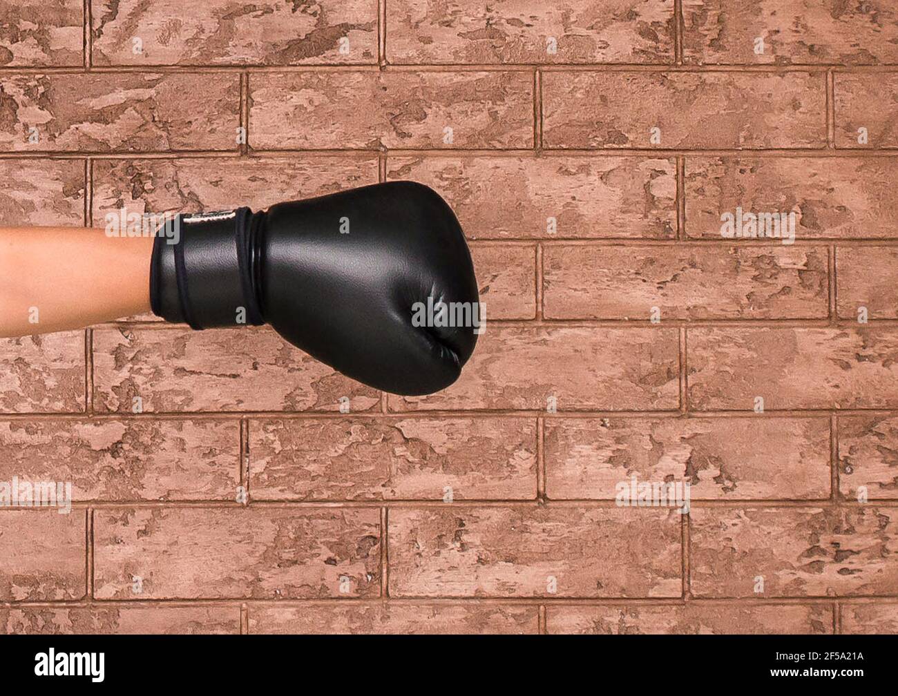 The hand of a guy in a black wrestling glove on a background of a brown brick wall. Boxing concept. Stock Photo