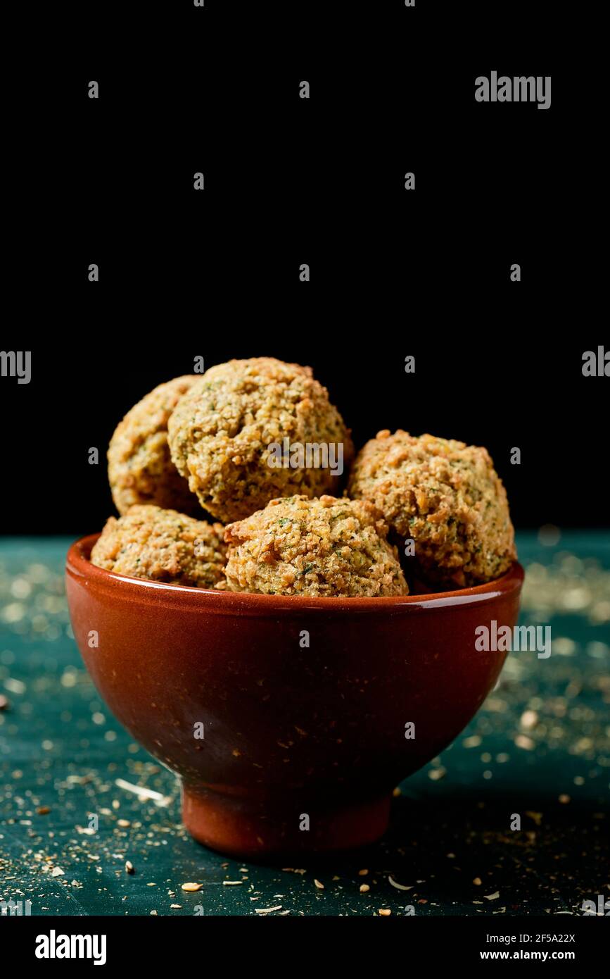 some falafel in an earthenware bowl, on a rustic green wooden table, against a black background Stock Photo