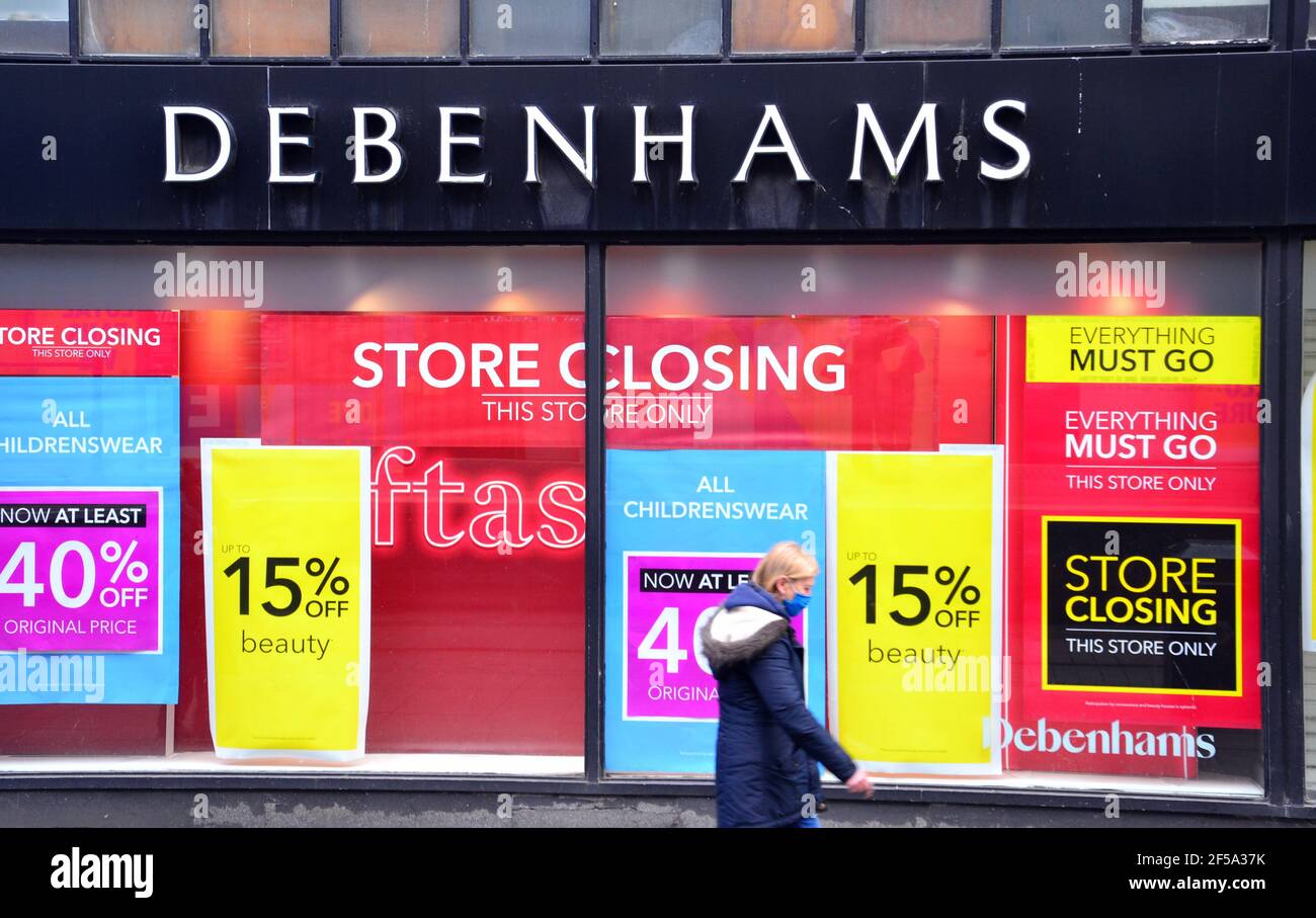 A woman walks past a window of a Debenhams store in Manchester, Greater Manchester, England, United Kingdom, which displays 'store closing' posters Stock Photo