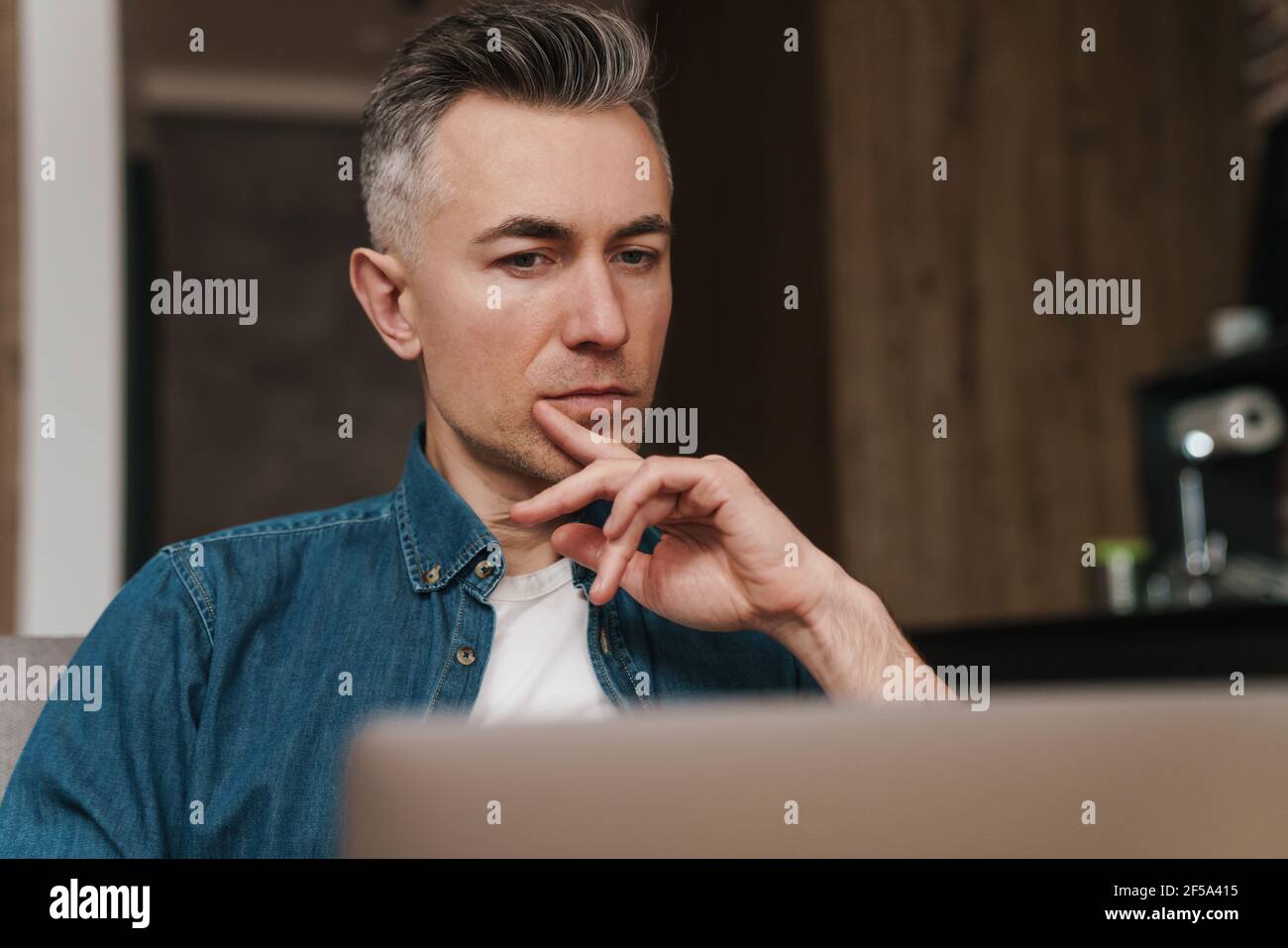 Focused handsome man using laptop while sitting on couch at home Stock Photo