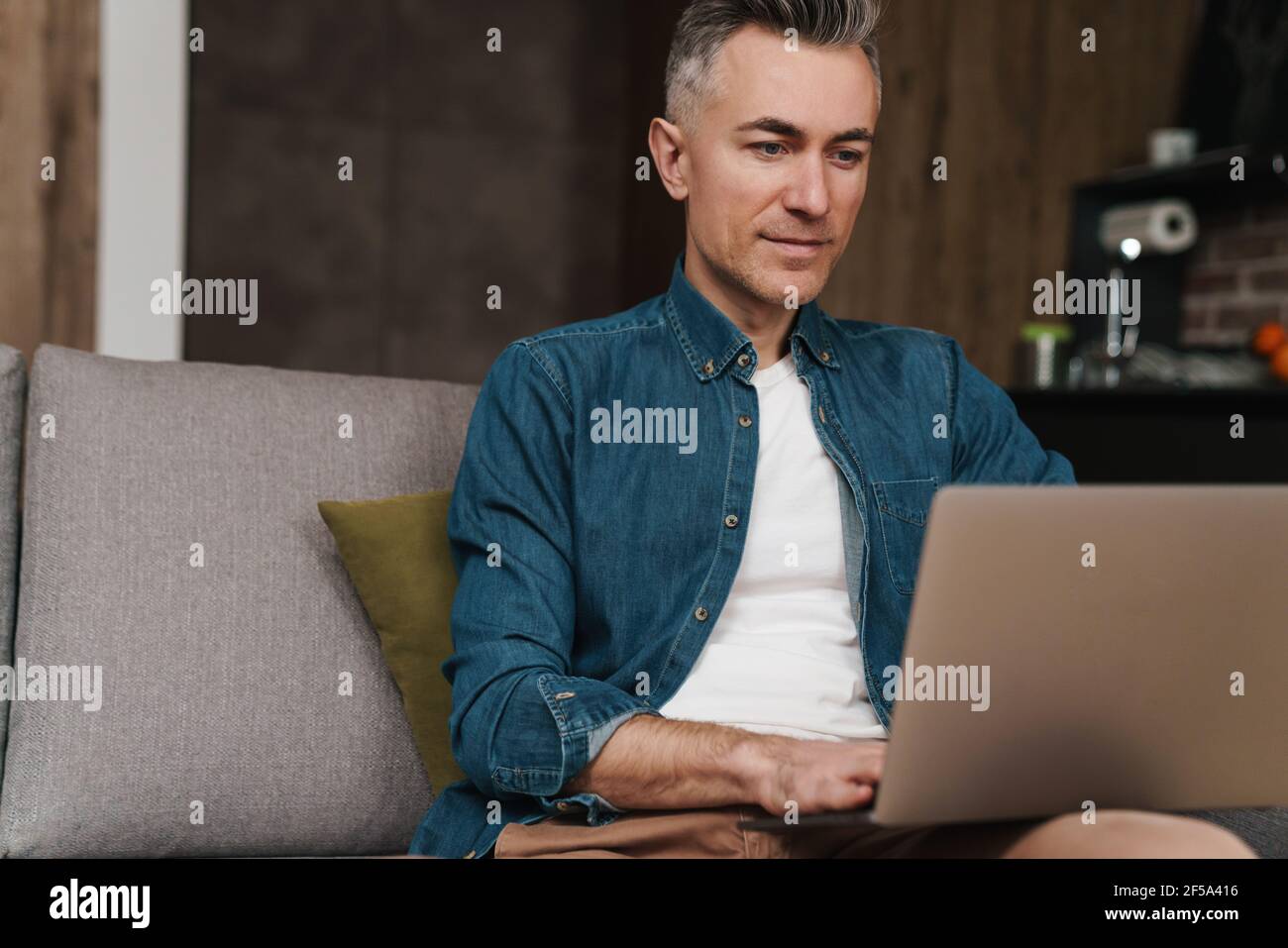 Pleased handsome man using laptop while sitting on couch at home Stock Photo
