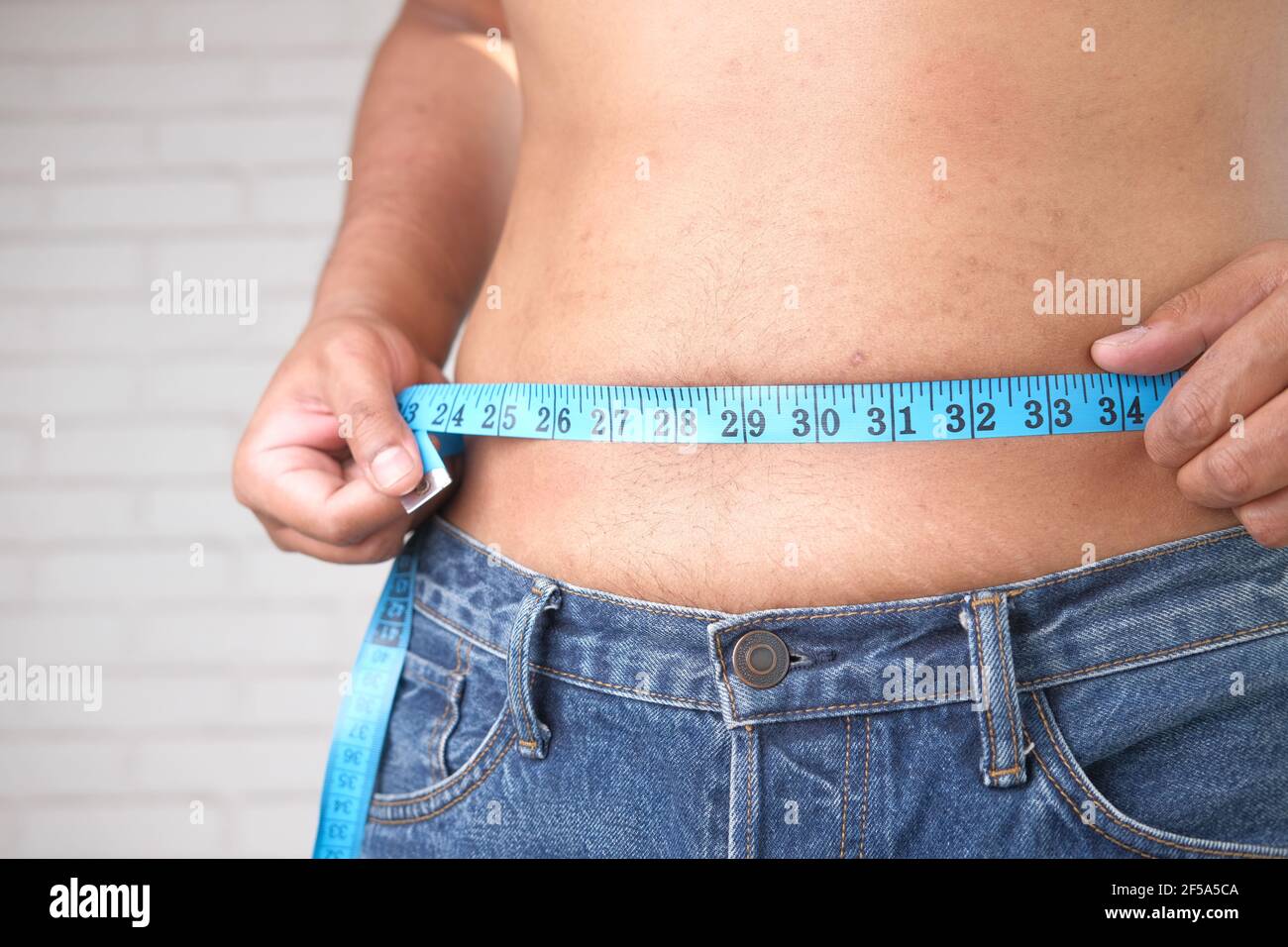 young man measuring his waist with a tape measure, close up. Stock Photo