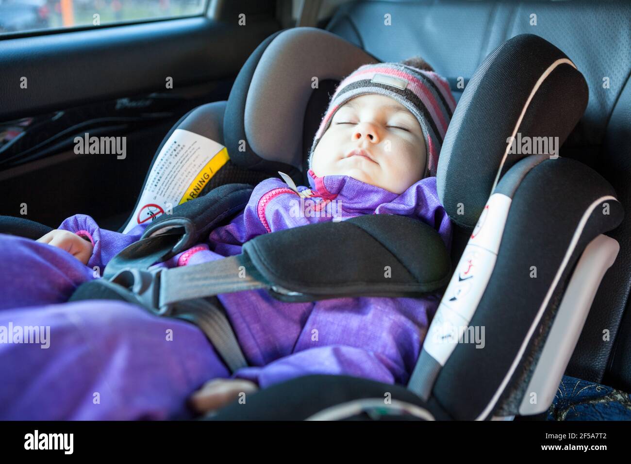 Sweet toddler girl sleeping peacefully in a car safety seat at winter season, warm clothing Stock Photo