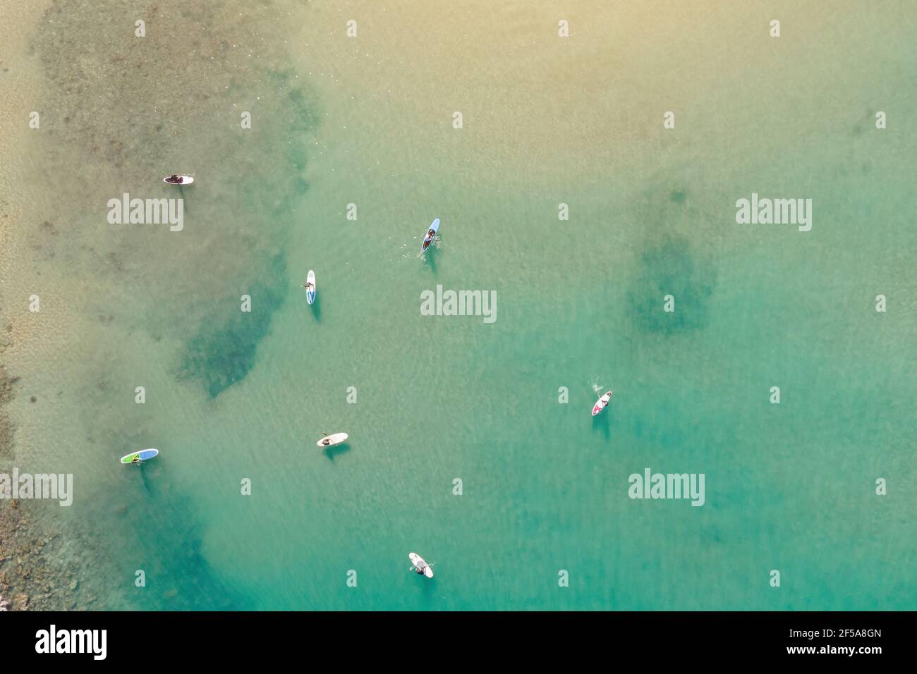 Aerial view by drone of people practicing Stand Up Paddle or SUP in Mediterranean turquoise clear sea. Stock Photo