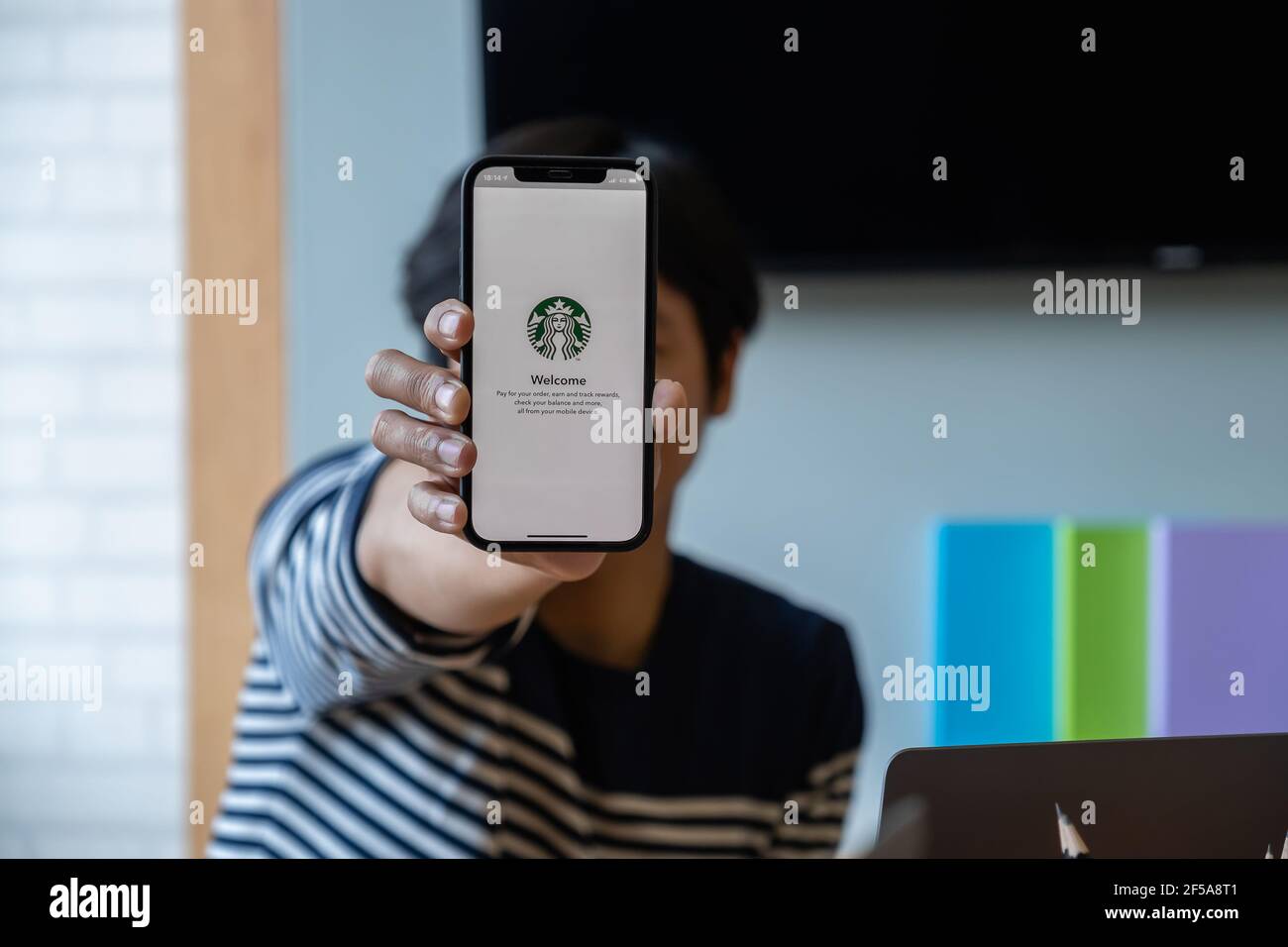 Chiang Mai, Thailand : Mar 19 2021 : Asian man showing Starbucks logo on iPhone screen in Starbucks coffee shop Stock Photo