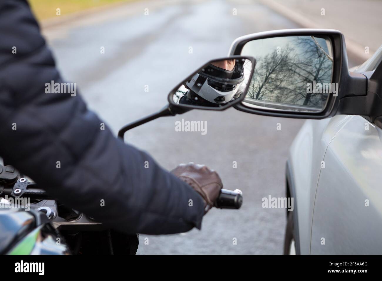Motorcyclist does not keep distance while riding side by side with a car, side mirrors are touching Stock Photo