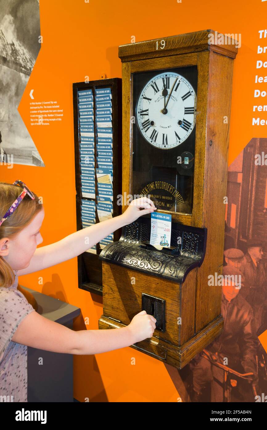 Child visitor girl tourist operating a clocking in on clock off machine at the Steam, Steel and Submarines exhibition display at Historic Dockyard / Dockyards Chatham in Kent. UK (121) Stock Photo