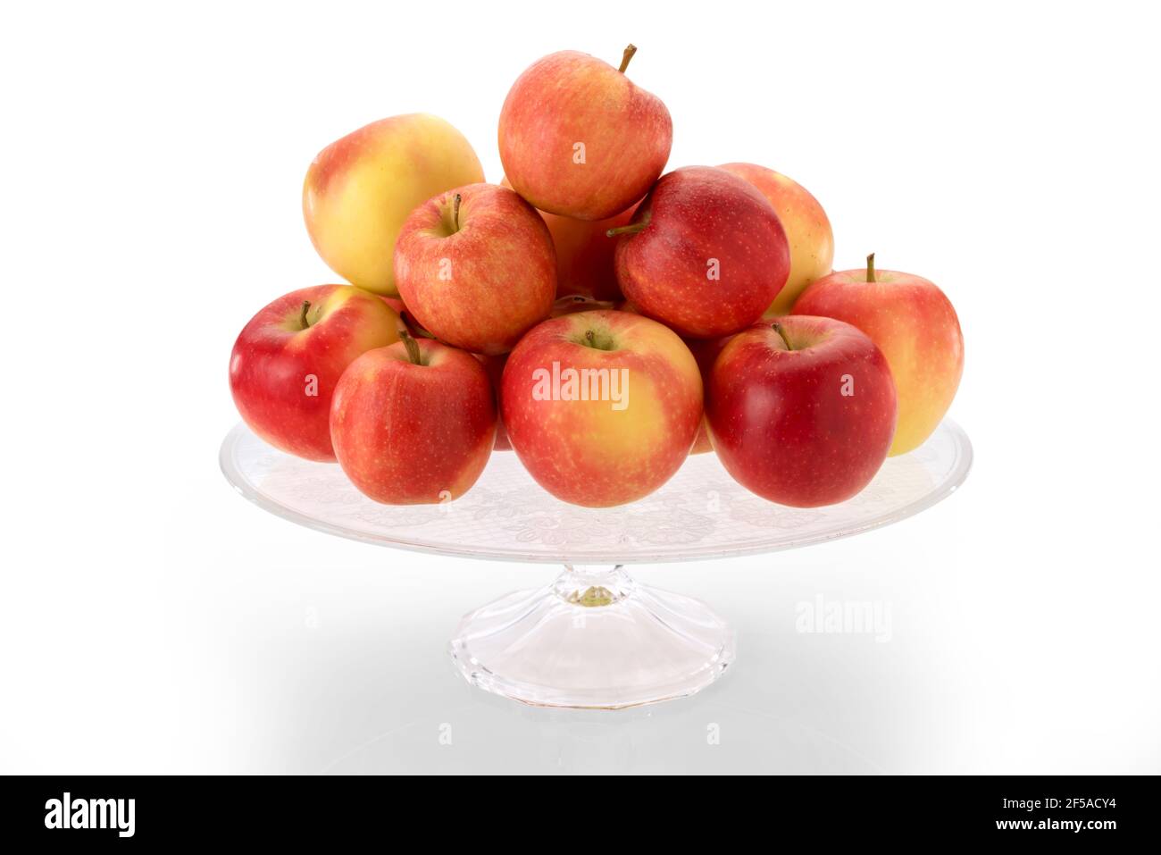 fuji apples on clear glass raised plate, red and yellow fruits isolated on white background Stock Photo