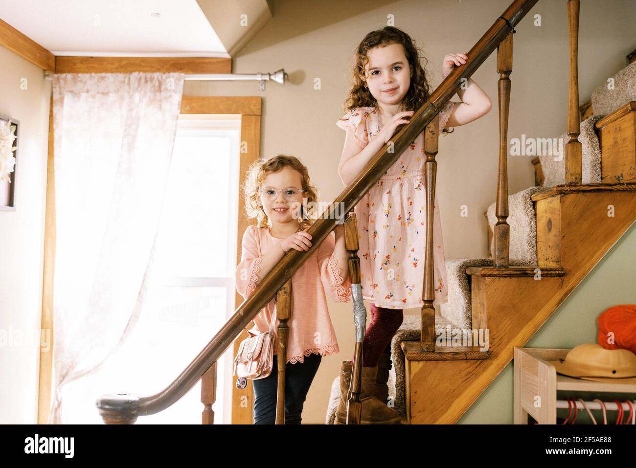 Big and little sister standing on wooden stair case together smiling Stock Photo