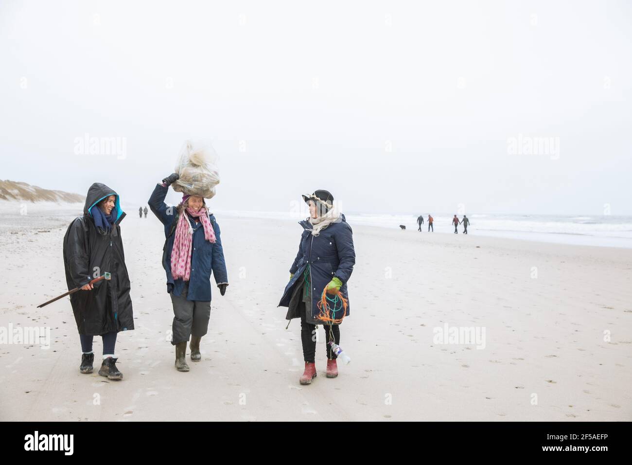Three Friends Carrying Trash On Beach Along North Sea in Denmark Stock Photo