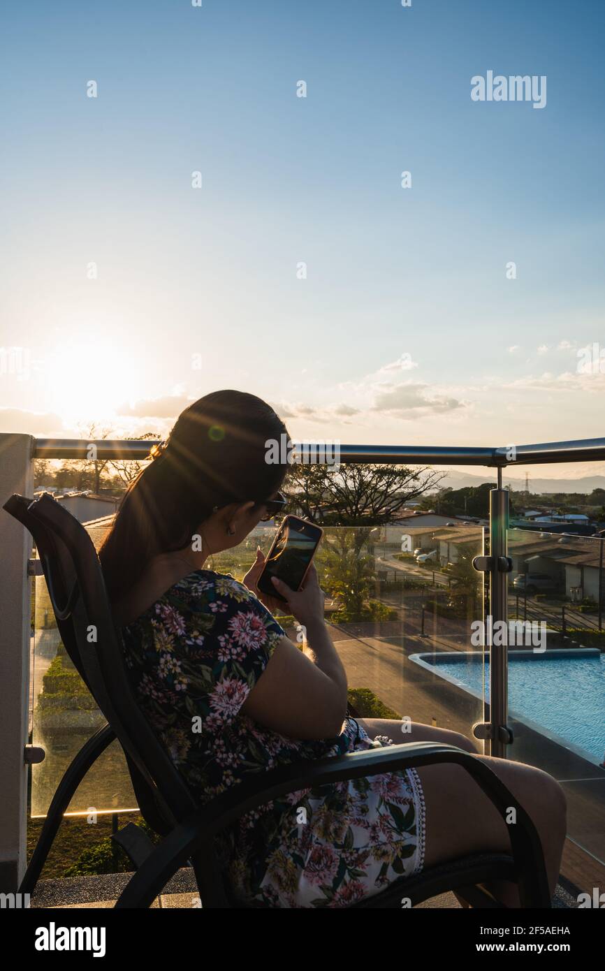 Unrecognizable woman taking a picture of the sunset in a balcony Stock Photo