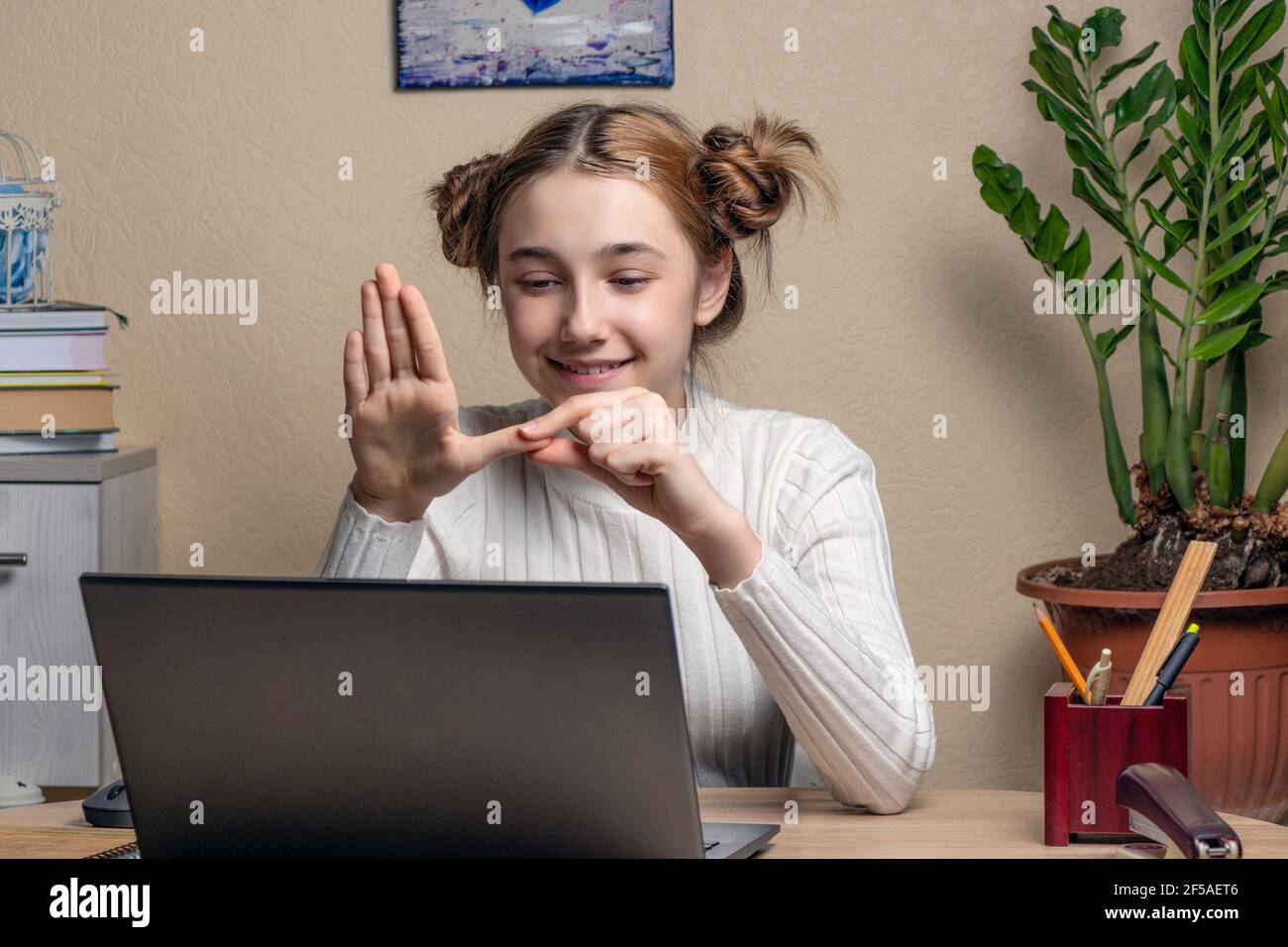 Smiling teenage girl deaf disabled child school girl learning online class on laptop communicating with a teacher by video conference call using sign la Stock Photo