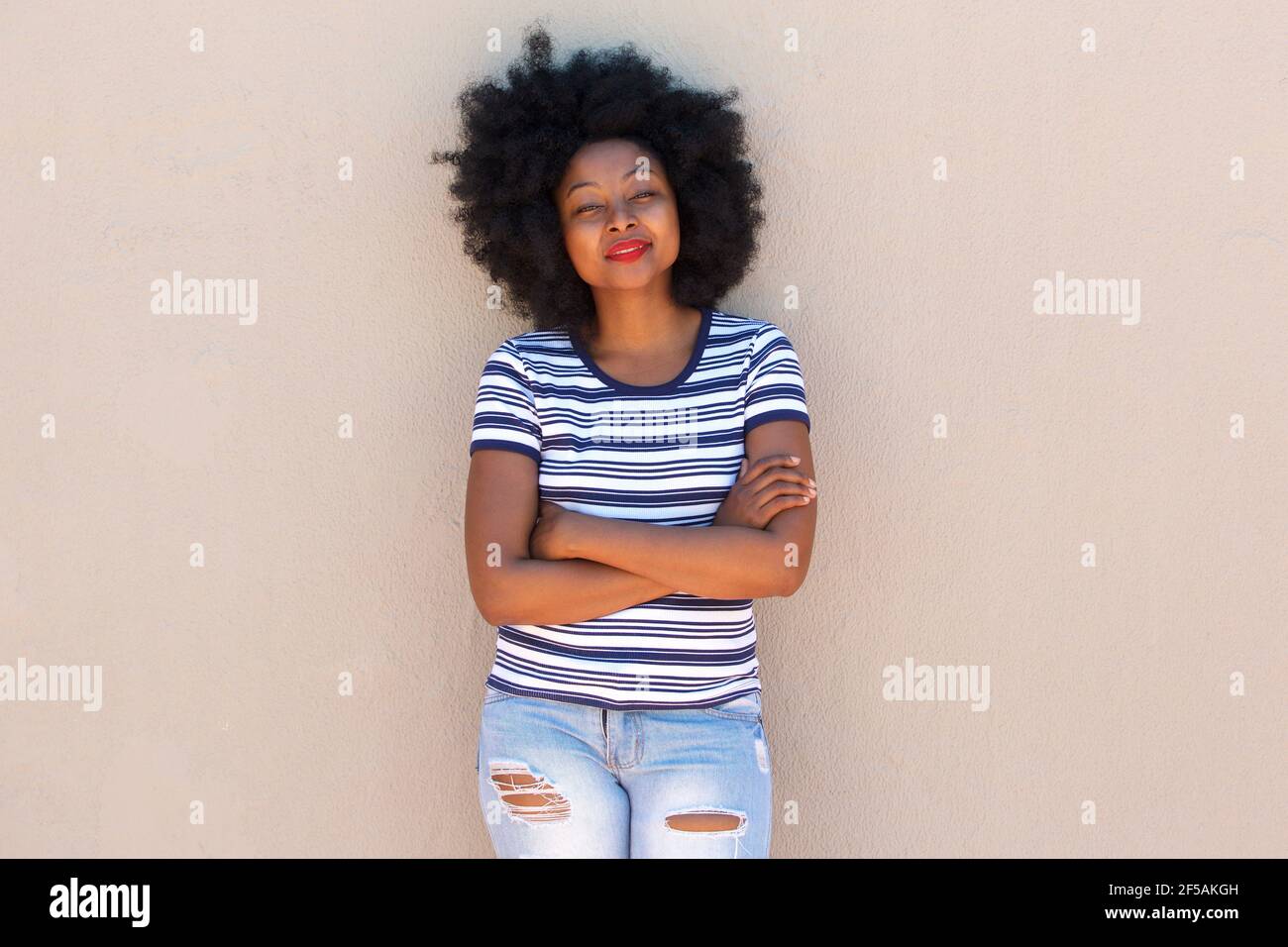 Portrait of beautiful young black woman standing with arms crossed by ...