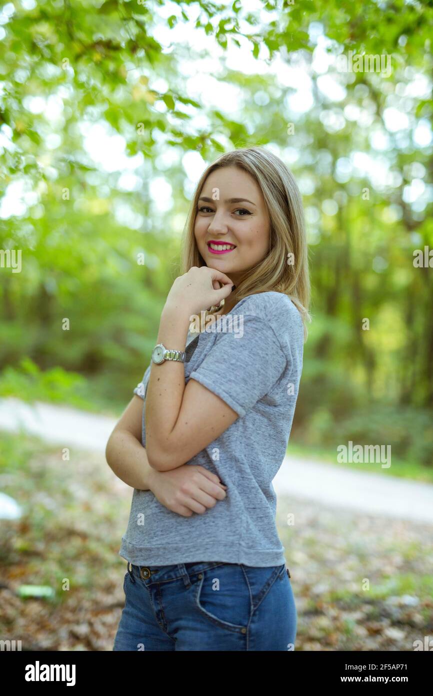 vertical shot of a smiling caucasian female standing posing against green trees 2F5AP71