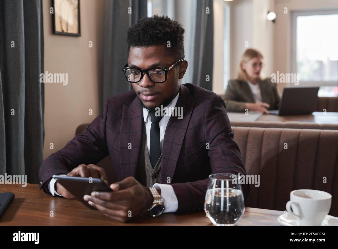 African young businessman using digital tablet while sitting at the table during lunch in cafe Stock Photo
