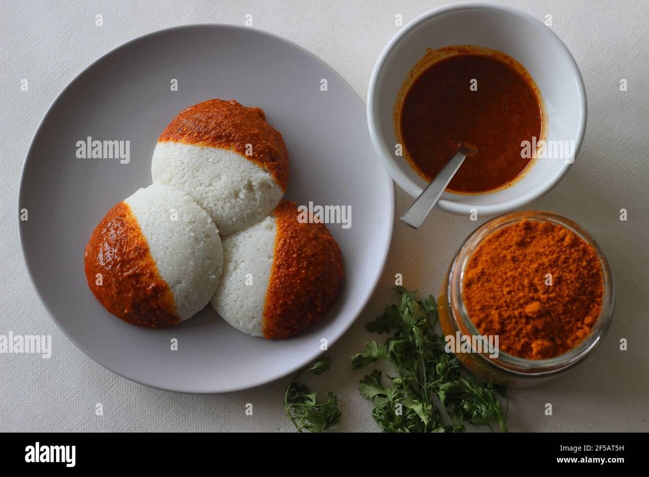Idli half covered with podi chutney also named gunpowder. Podi is made