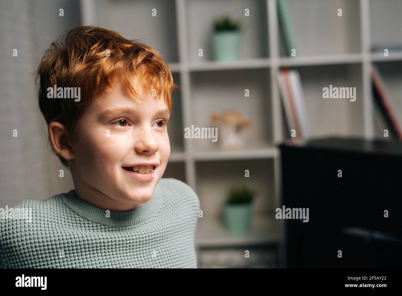 Close-up portrait of cheerful freckled redhead child boy sitting on table and looking away Stock Photo