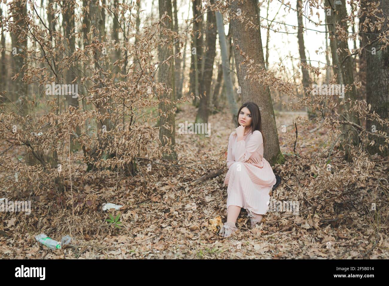 Young caucasian female in a delicate pink dress posing sitting under a ...