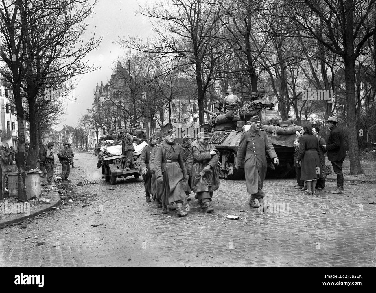 Cologne, Germany 1945 American troops escort captured German soldiers after they surrendered watched by local people during World War Two following heavy bombing of the city. WW2 second world war. german defeat allied victory Deutschland 1940s surrender Europe European history destruction Stock Photo