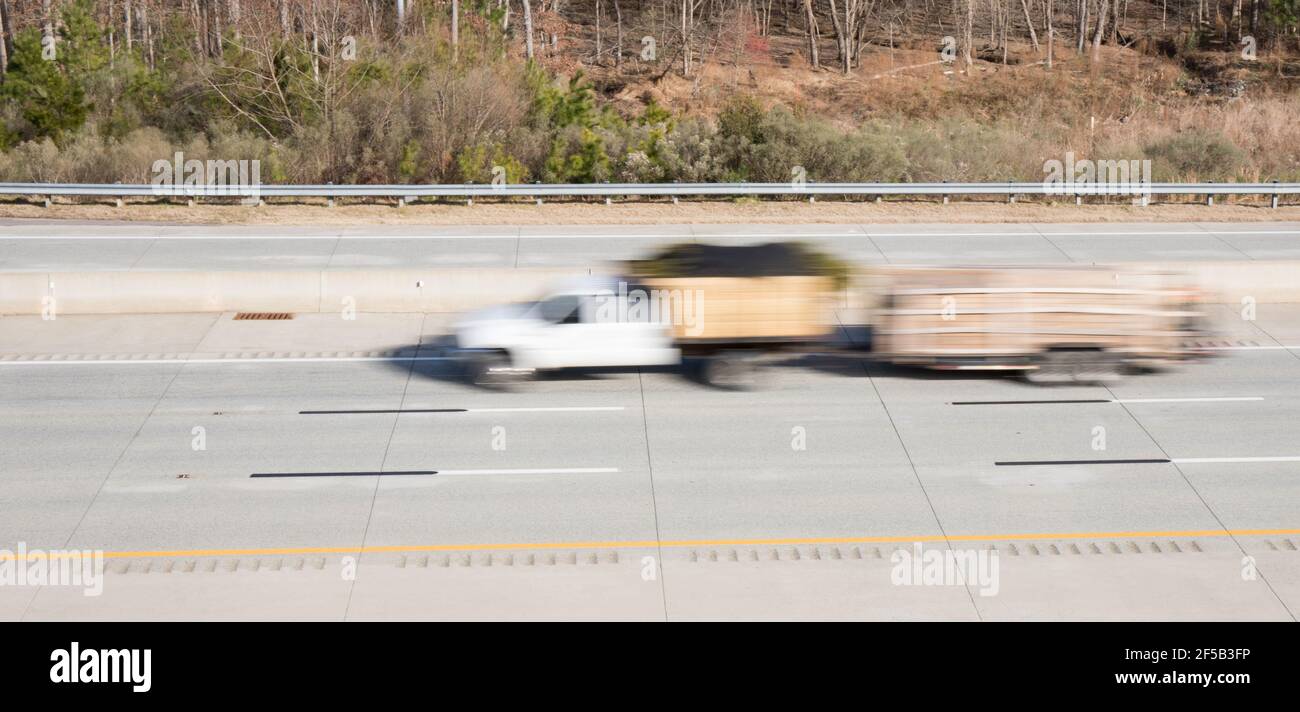 A white landscaping truck pulling a trailer in blurred motion on a highway showing movement while the rest of the shot is in focus. Stock Photo