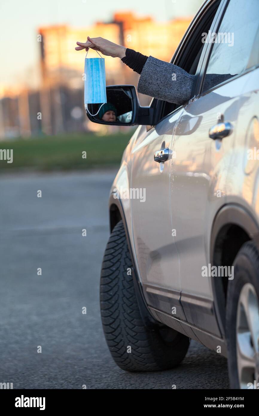 Woman holding new medical mask in her hand, stretching her hand through a car window Stock Photo