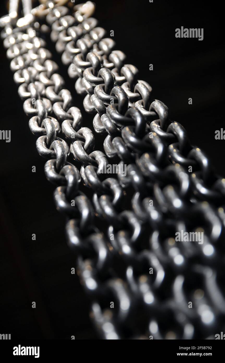 Metal chains dangling and illuminated with bright light. Industry Stock